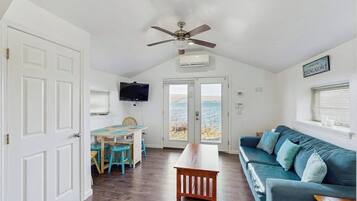 A room with a ceiling fan, a television mounted on the wall, a large window with a view, and a blue sofa.