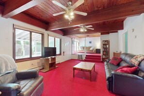 A spacious living room with a red carpet, leather sofas, a wooden coffee table, ceiling fans, and a television.