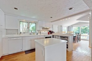 A modern kitchen with white cabinetry, a central island, and a dining area with chairs.