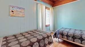 Ein Zimmer mit zwei Betten, einem Wandbild, einem Fenster mit Vorhängen und einem Deckenventilator.