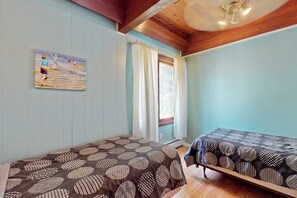 A room with two beds, a painting on the wall, a window with curtains, and a ceiling fan.