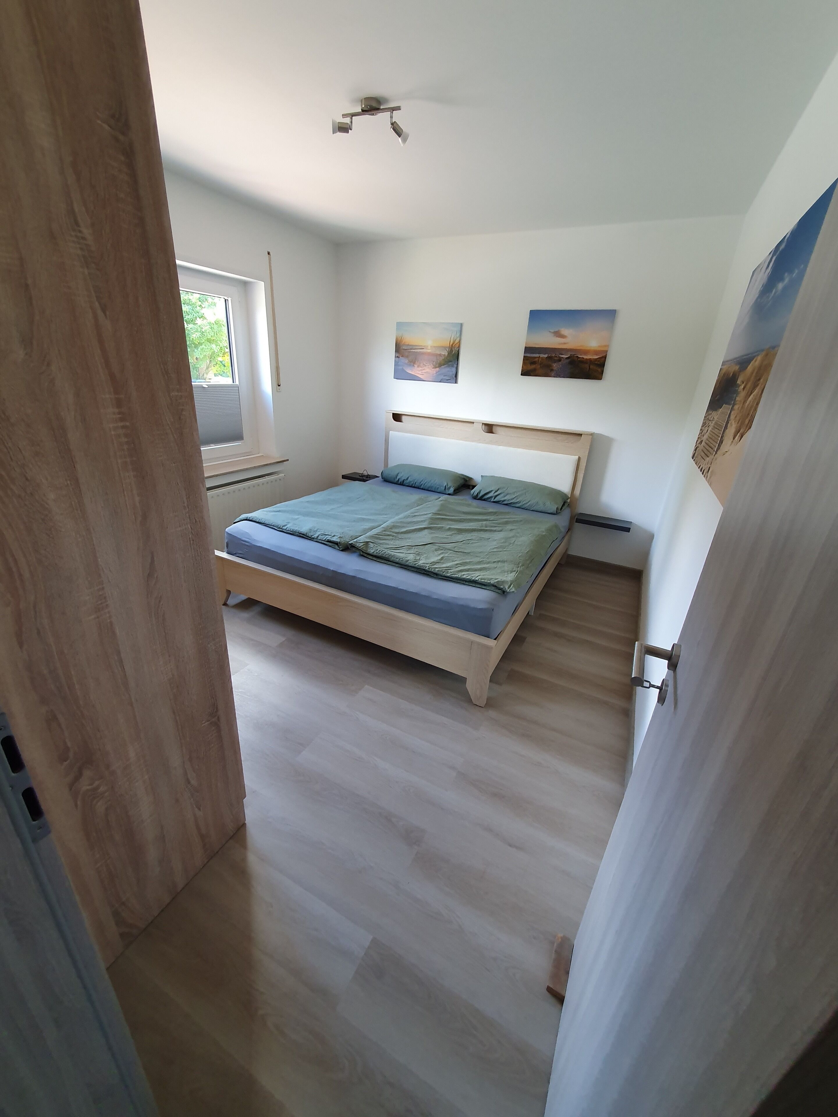 Un dormitorio con cama, ventana y dos cuadros colgados en la pared.
