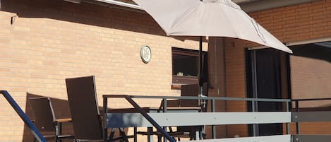 Un patio exterior con mesa y sillas, un área de estar techada y un edificio de ladrillo al fondo.