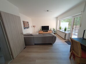 A modern living room with a sectional sofa, a flat-screen TV, and a dining area with a table and chairs.