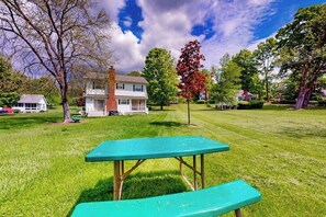 A picnic table in a grassy area with houses in the background. - 4BR home with grill, close to town & lake (Queensbury)