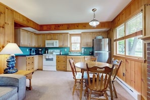 A kitchen with wooden cabinets, a dining table with chairs, a refrigerator, and a microwave. - 4BR home with grill, close to town & lake (Queensbury)
