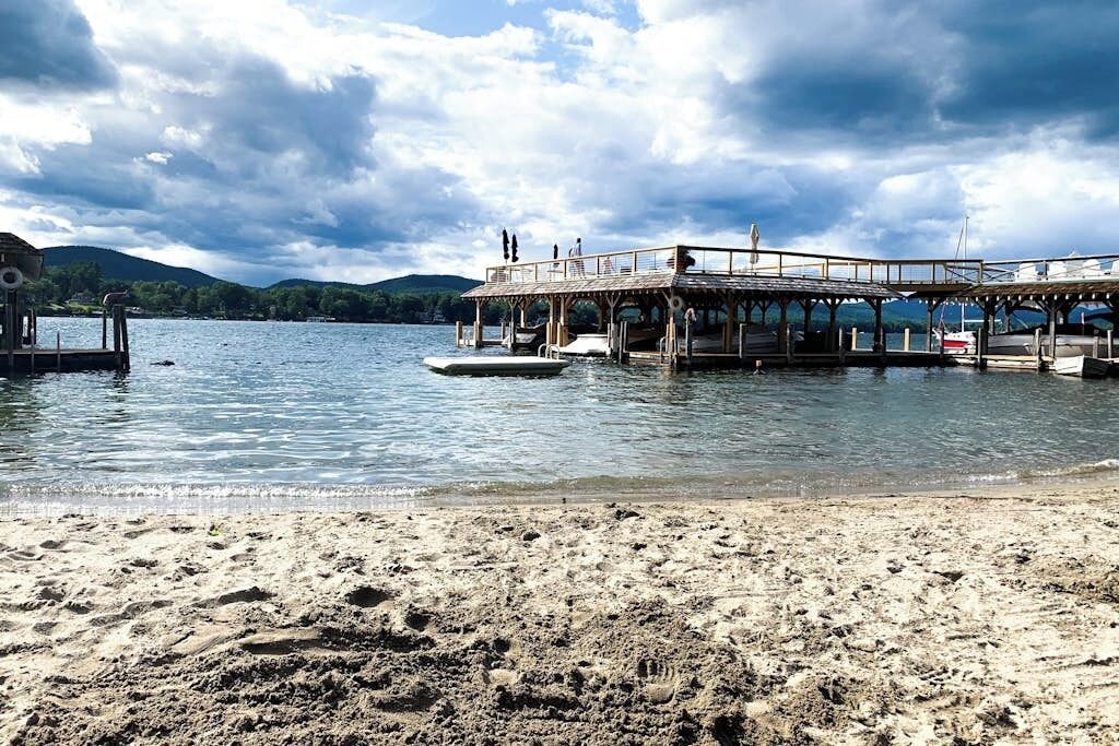 A beach with a wooden pier extending into calm water, surrounded by hills.