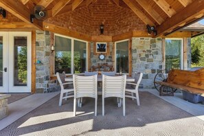 Eine überdachte Terrasse mit einer Steinmauer, Holzbalkendecke und einem Tisch mit Stühlen.