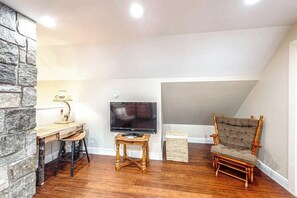 Ein gemütliches Zimmer mit Schreibtisch aus Holz, einem Fernseher und einem bequemen Sessel.