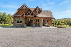Ein zweistöckiges Haus mit Natursteinfassade und Holzbalkonen, einer Veranda und einer Auffahrt.