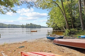 A lakeside setting with boats, a sandy shore, and a forested background. - Beautiful 5BR Lakefront Adirondacks - Dock (Chestertown)