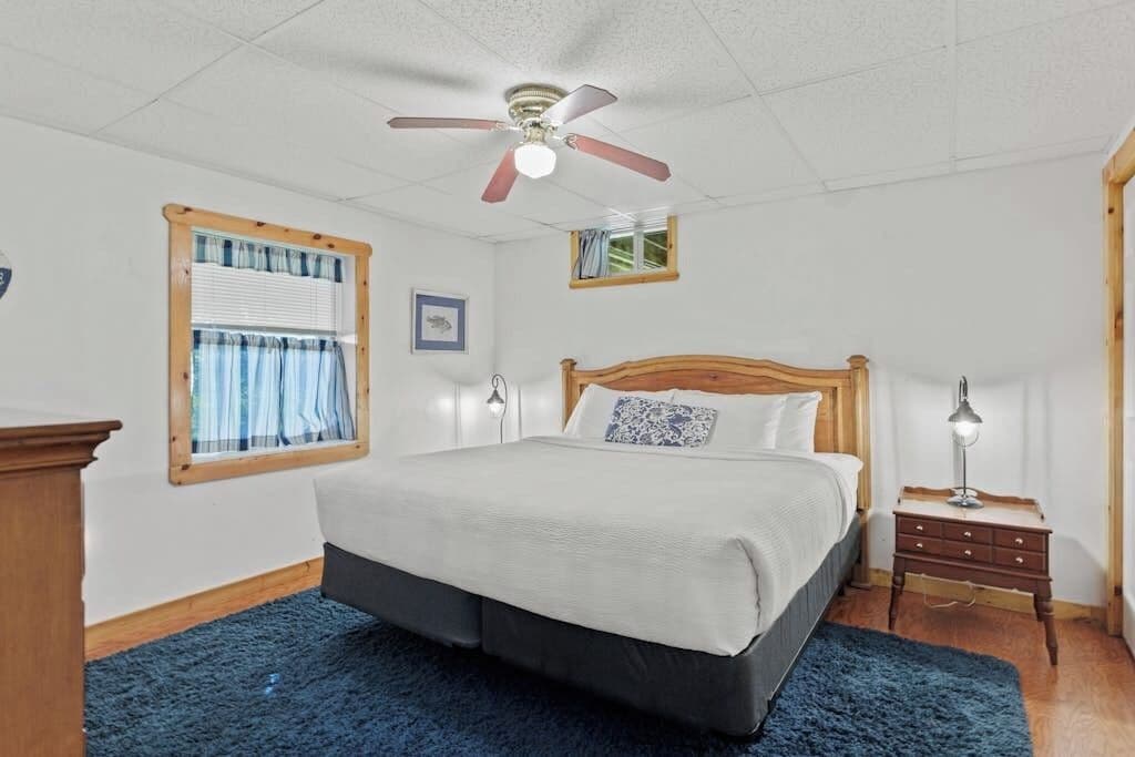A bedroom with a bed, a ceiling fan, a nightstand, and a window with curtains.