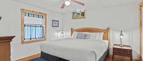 A bedroom with a bed, a ceiling fan, a nightstand, and a window with curtains.