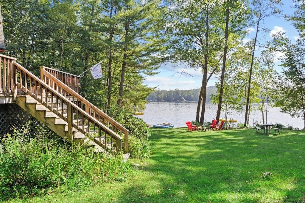 A wooden deck leading to a grassy area with a lake view, outdoor furniture, and a boat dock.