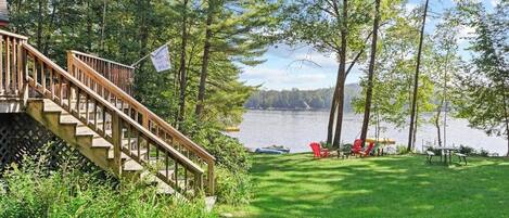 A wooden deck leading to a grassy area with a lake view, outdoor furniture, and a boat dock.