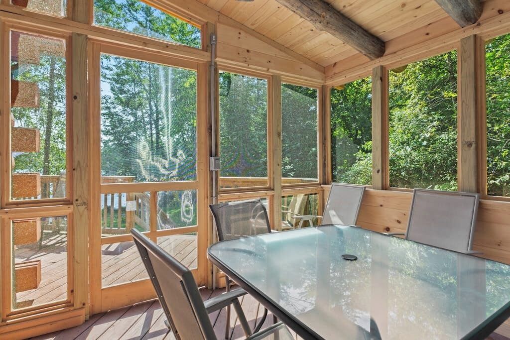A covered outdoor dining area with a glass table and chairs, surrounded by large windows.