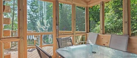 A covered outdoor dining area with a glass table and chairs, surrounded by large windows.