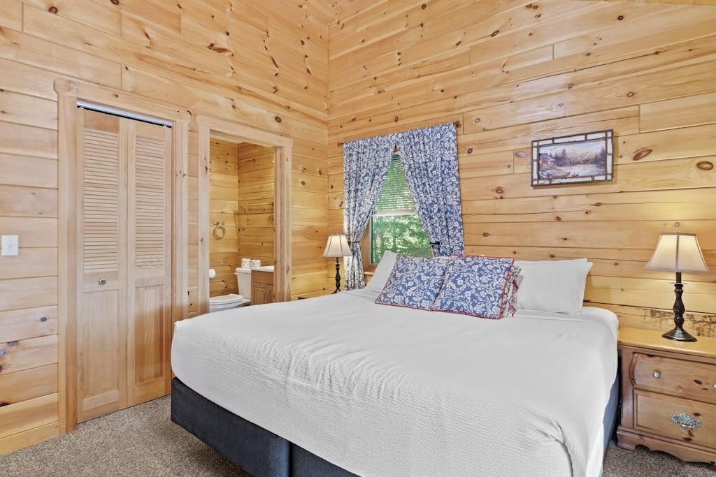 Een slaapkamer met houten lambrisering, een bed, nachtkastjes en een raam met gordijnen.
