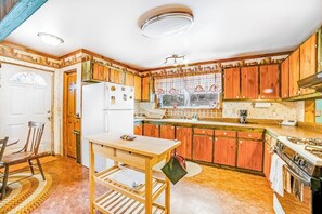 A kitchen with wooden cabinets, a refrigerator, a stove, and a dining area with a table and chairs. - Dog-friendly 2BR cabin with mountain view (Indian Lake)
