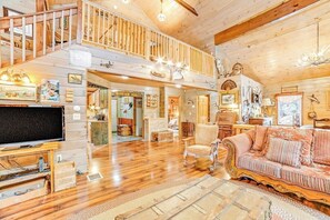 A spacious loft-style room with a wooden staircase, a cozy seating area with a sofa and armchairs, and a television. - Dog-friendly 2BR cabin with mountain view (Indian Lake)