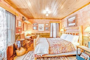 A cozy room with a wooden bed, a small table, and a chair. There is a window with curtains and a wall with framed pictures. - Dog-friendly 2BR cabin with mountain view (Indian Lake)