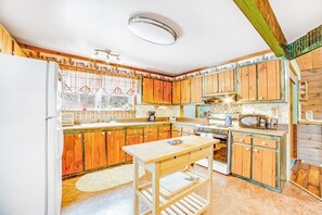 A kitchen with wooden cabinets, a central island, a refrigerator, and a window with curtains. - Dog-friendly 2BR cabin with mountain view (Indian Lake)