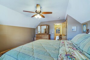 Ein Schlafzimmer mit einem Bett, einem Deckenventilator, einer Kommode und einer Tür zu einem anderen Raum.