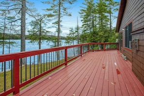 Eine Holzterrasse mit roter Brüstung, die auf einen See mit umliegenden Bäumen blickt.