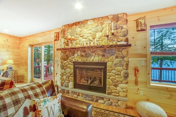 Un intérieur de chalet chaleureux avec une cheminée en pierre, des murs en bois et une vue sur l’extérieur.