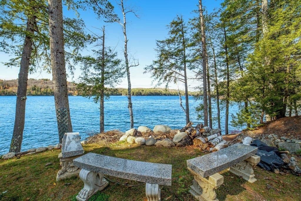 A lakeside setting with two stone benches, a pile of rocks, and a clear view of the water.