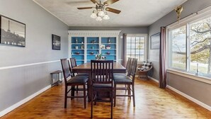 Un comedor con una mesa de madera, sillas, un ventilador de techo y vistas amplias por las ventanas.