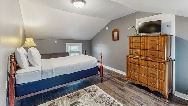 Un dormitorio con cama, cómoda, televisor y ventana.