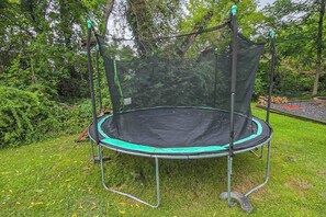 A trampoline with a safety net, surrounded by grass and trees.
