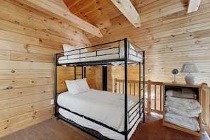 A bunk bed room with wooden walls and a ceiling, a small table with a lamp, and a shelf with folded towels. - 3BR cabin home withlake views, soaking tub - dogs ok (Dundee)