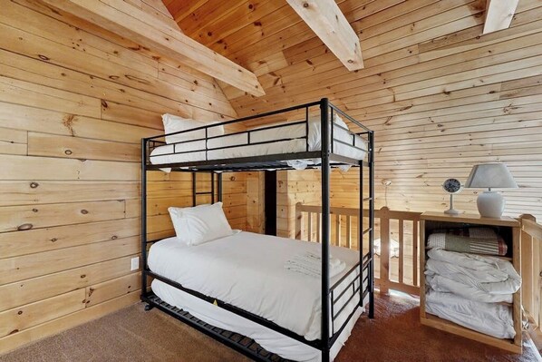 A bunk bed room with wooden walls and a ceiling, a small table with a lamp, and a shelf with folded towels. - 3BR cabin home withlake views, soaking tub - dogs ok (Dundee)