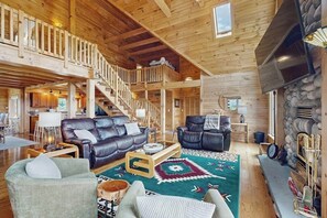 A spacious log cabin interior with a living room, a staircase, and a stone fireplace. - 3BR cabin home withlake views, soaking tub - dogs ok (Dundee)
