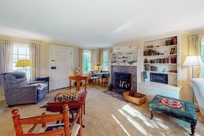 A cozy living room with a fireplace, a chess table, and a bookshelf. - 6BR country retreat with game room & large yard (Penn Yan)