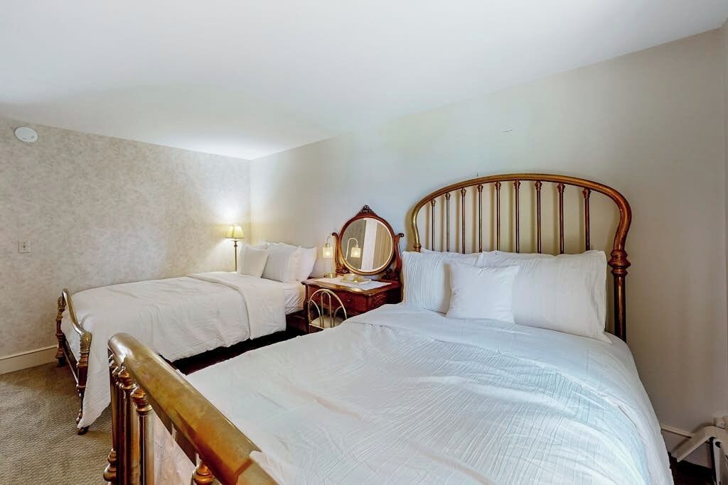 Ein Hotelzimmer mit zwei Einzelbetten, einem Nachttisch mit Lampe, einem Spiegel und einem Holz-Kopfteil.