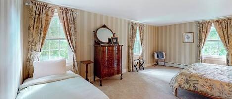 Un dormitorio con dos camas, un tocador, un espejo y cortinas.