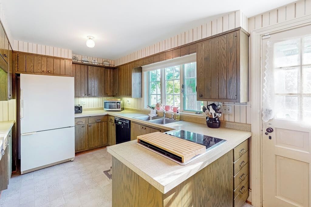 Una cocina con armarios de madera, un refrigerador blanco, un microondas y un lavamanos.