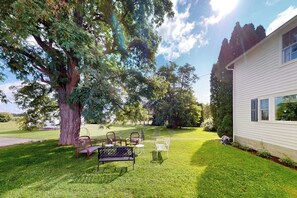 A well-maintained lawn with outdoor furniture, a large tree, and a house with a white exterior. - 6BR country retreat with game room & large yard (Penn Yan)