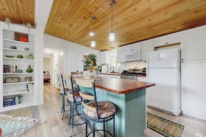 Una cocina con armarios blancos, techo de madera y una isla central con taburetes de bar.