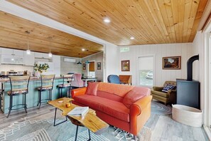 Un interior moderno con techo de madera, una zona de cocina, un salón con sofá rojo y una chimenea.