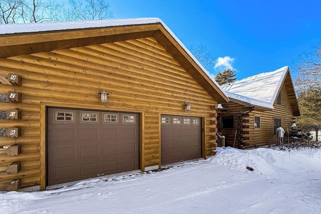 A log cabin with two garage doors and a snow-covered roof.