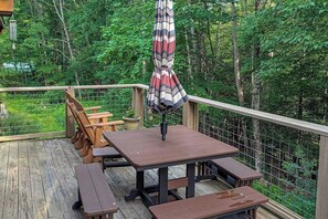 A wooden deck with picnic tables and an umbrella, surrounded by a wire fence and dense greenery. - 3BR house, dog-friendly, gas fireplace, bbq, withd (Hague)