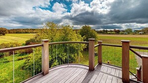 A wooden deck with a railing overlooking a green landscape and a cloudy sky. - 1BR home w/deck, countryside views & close to town (Penn Yan)
