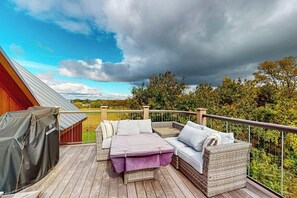 Ein überdachter Außenbereich mit einer Sitzecke, inklusive Sofa und Tisch, einem Grill und Blick auf die umliegende Landschaft.