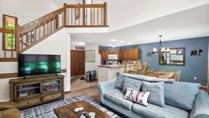 Un salon comprenant un canapé, une table basse et un téléviseur. Un escalier mène à l’étage supérieur.