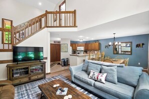 Ein Wohnzimmer mit Sofa, Couchtisch und Fernseher. Eine Treppe führt auf eine obere Ebene.