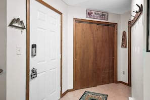 A hallway with a wooden door, a welcome sign, a coat rack, and a 'Gone Skiing' sign.